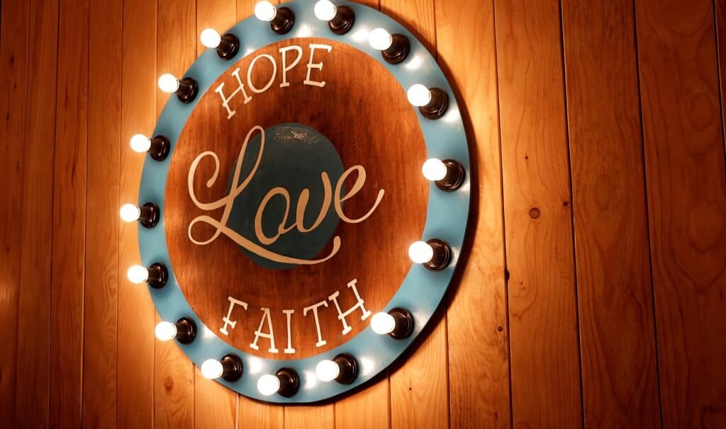 A vibrant circular sign with 'Hope, Love, Faith' illuminated by bulbs on a wooden wall.
