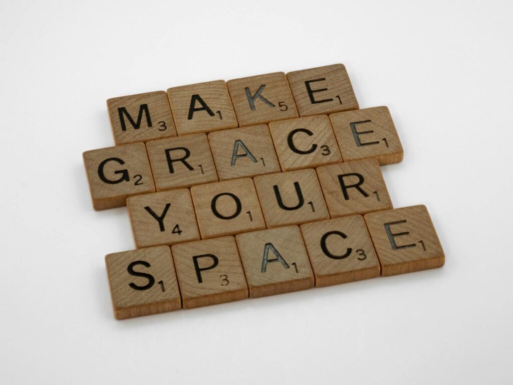 Close-up of wooden Scrabble tiles spelling 'Make Grace Your Space' on a white background.