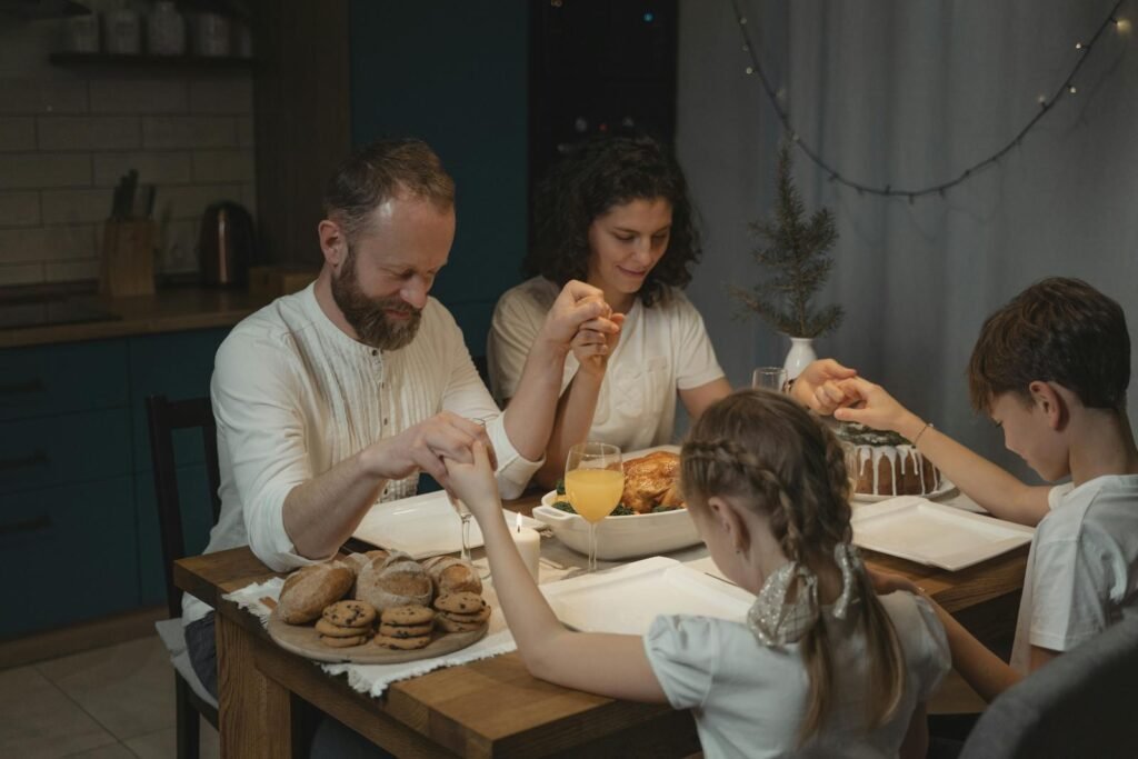 Family holding hands and praying over a dinner table with turkey and cookies during festival celebration, Simple Ways to Start Praying Daily